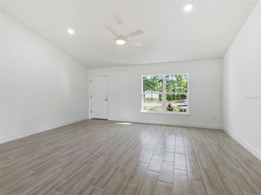 An empty room features white walls, a ceiling fan, and light-colored wood-look tile flooring — 4994 SW 166TH LOOP, OCALA, FL