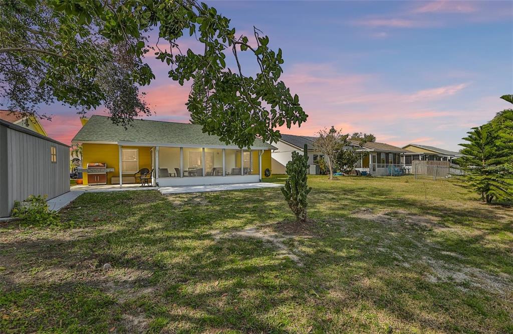 A yellow house with a screened-in patio sits in a large, grassy backyard at sunset — 128 LOOKOUT DRIVE, APOLLO BEACH, FL
