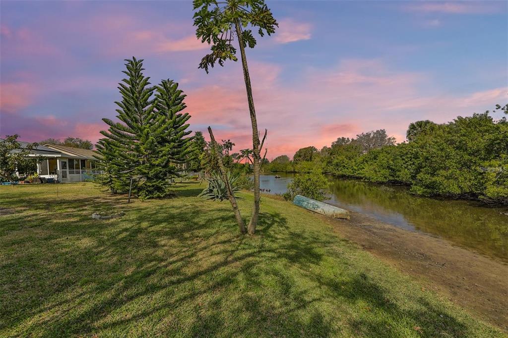 A grassy backyard leads to a narrow waterway with a small boat on the shore — 128 LOOKOUT DRIVE, APOLLO BEACH, FL