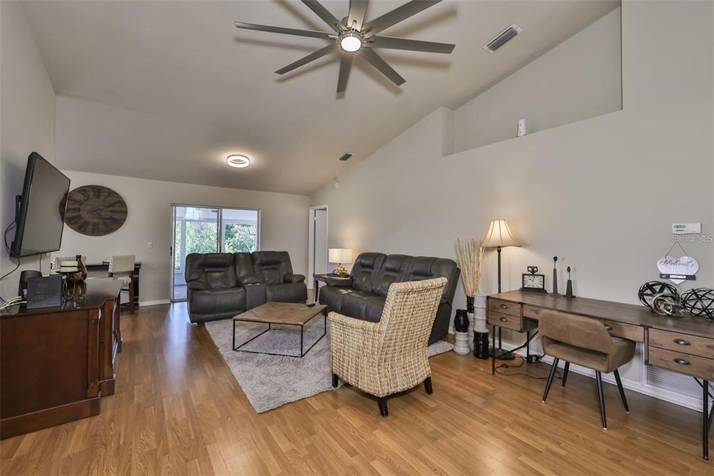 A living room features wood flooring, a ceiling fan, leather furniture, and a desk area — 128 LOOKOUT DRIVE, APOLLO BEACH, FL