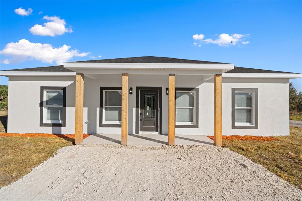 A single-story house with a white stucco exterior, dark window trim, and four wooden porch posts — 17428 NW 288TH STREET, OKEECHOBEE, FL