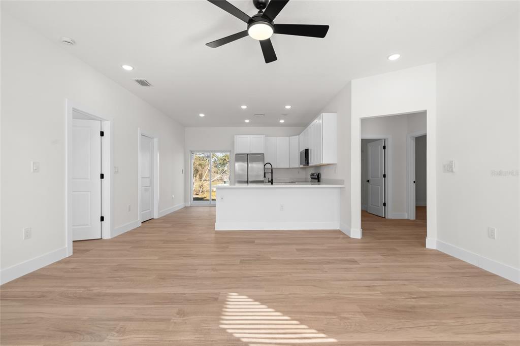 An open-concept kitchen and living area features white cabinetry, stainless appliances, and light wood flooring — 17428 NW 288TH STREET, OKEECHOBEE, FL