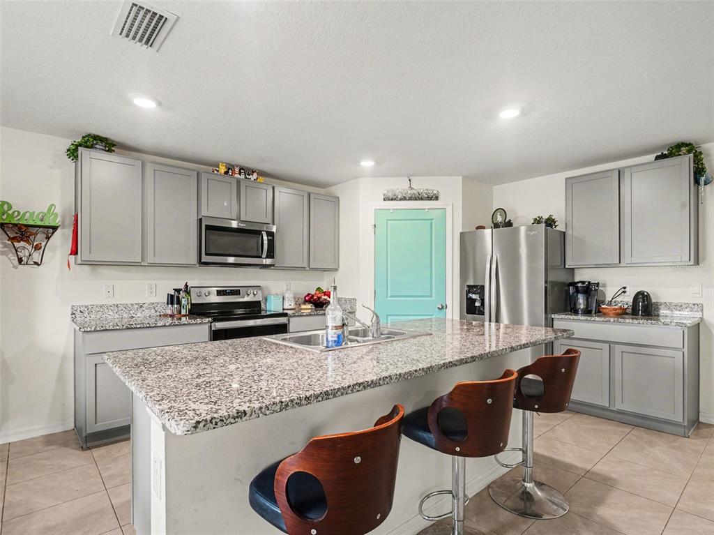 A kitchen features gray cabinets, granite countertops, a central island with bar stools, and stainless appliances — 4114 DOVETAIL LANE, PALMETTO, FL