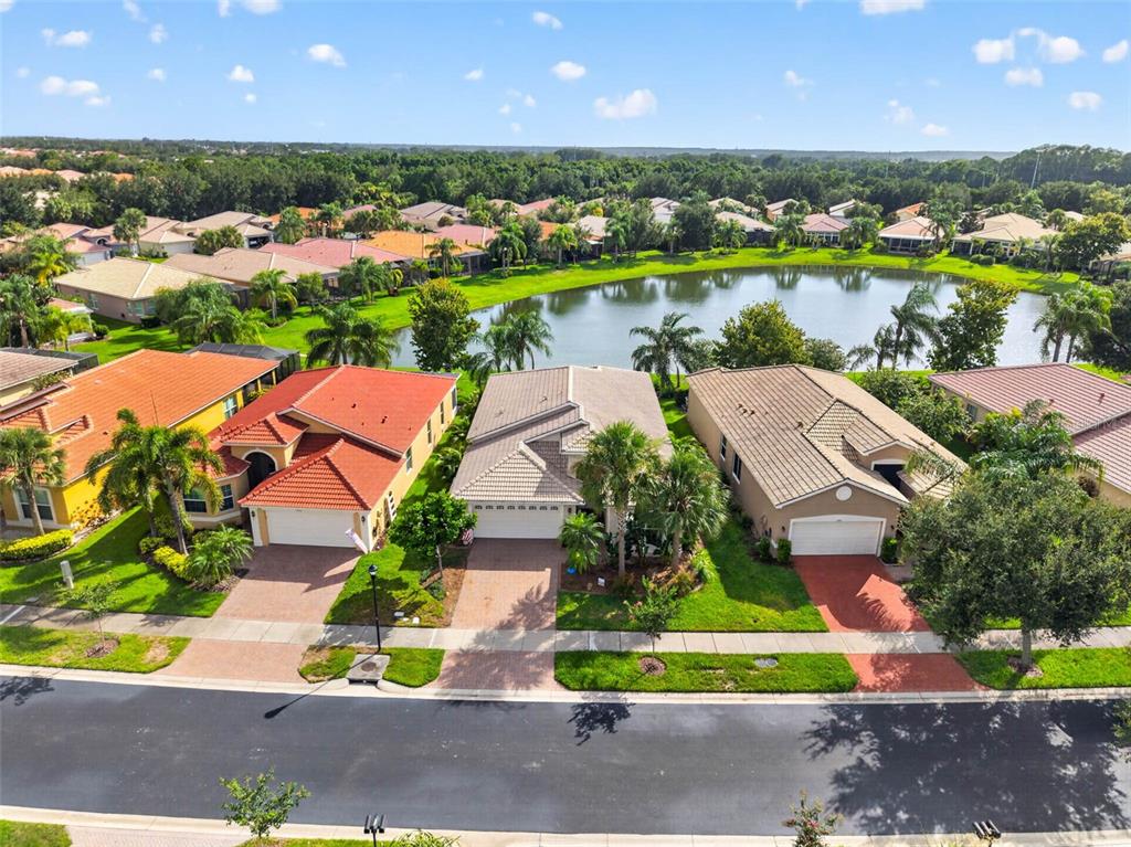 An aerial view shows three suburban houses with tiled roofs situated along a small lake — 15929 GOLDEN LAKES DRIVE, WIMAUMA, FL