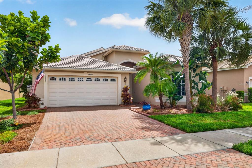 A single-story house with a beige stucco exterior, a tiled roof, and a brick driveway — 15929 GOLDEN LAKES DRIVE, WIMAUMA, FL