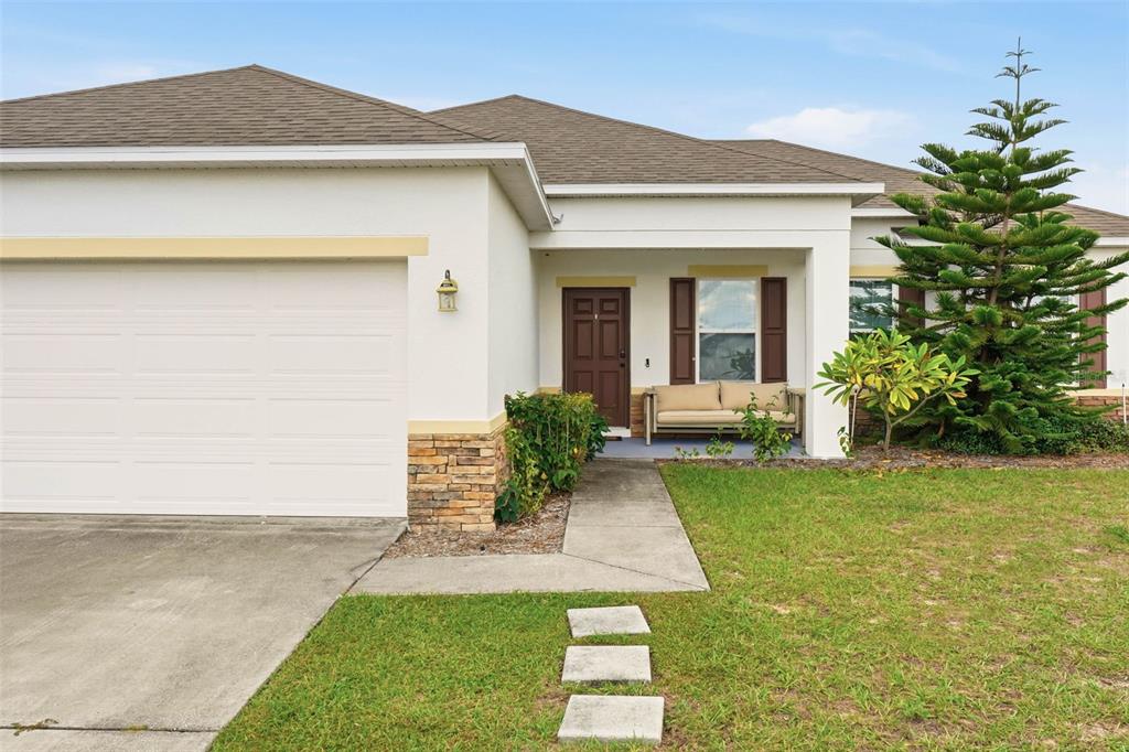 A single-story house with a white exterior, stone accents, a garage, and a front porch — 875 FRASER DRIVE, KISSIMMEE, FL