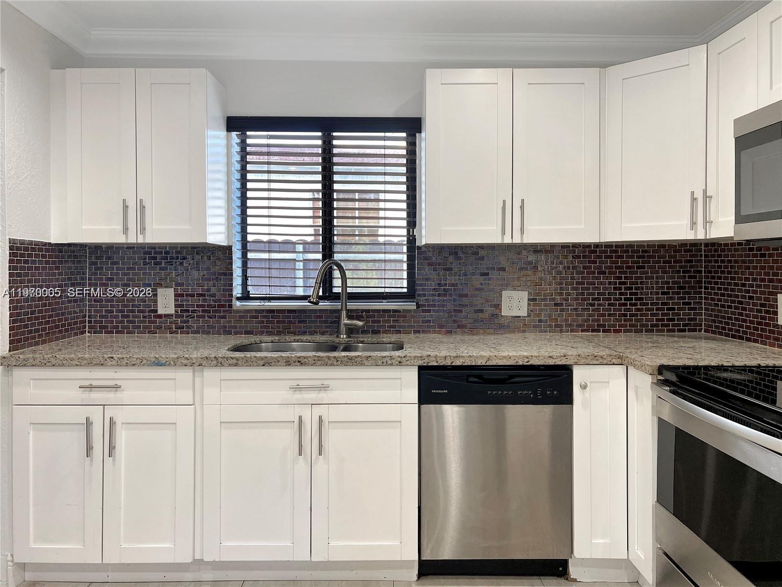 A kitchen features white cabinets, granite countertops, a stainless steel dishwasher, and dark tiled backsplash — 221 W 31st St, Hialeah FL 33012, HIALEAH, FL