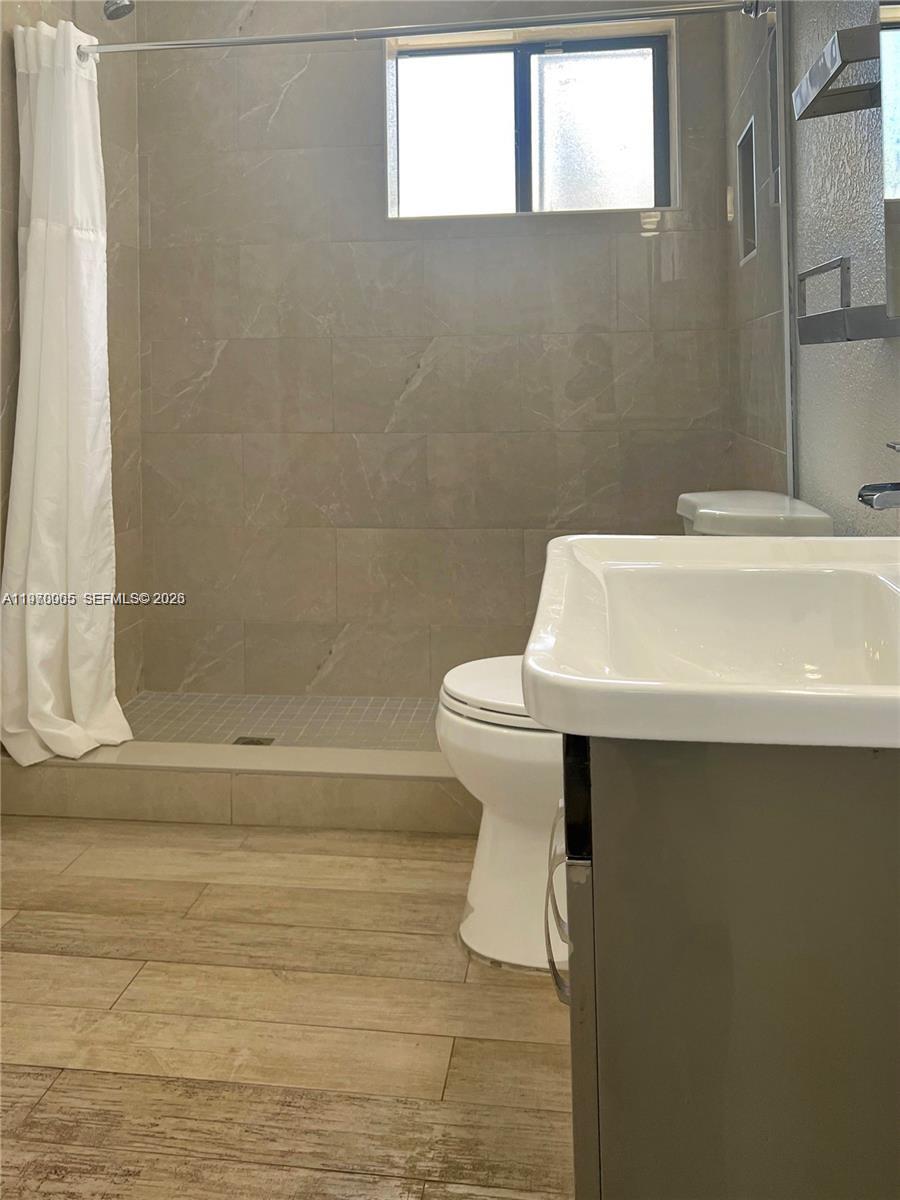 A bathroom features a tiled walk-in shower, a white toilet, and a vanity sink — 221 W 31st St, Hialeah FL 33012, HIALEAH, FL