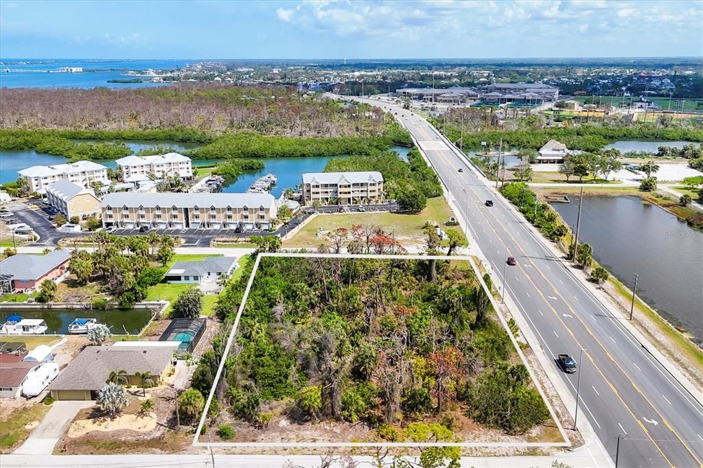 An aerial view shows a rectangular, wooded vacant lot situated next to a multi-lane road — 2440 PLACIDA ROAD, ENGLEWOOD, FL