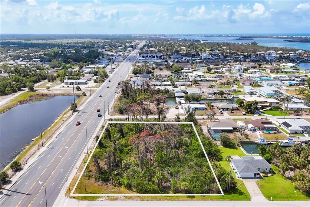 An aerial view shows a rectangular, wooded vacant lot adjacent to a multi-lane highway — 2440 PLACIDA ROAD, ENGLEWOOD, FL