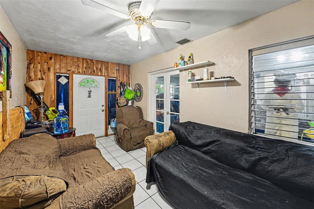 A living room features wood-paneled walls, tile flooring, a ceiling fan, and two sofas — 110 N JUPITER AVENUE, CLEARWATER, FL