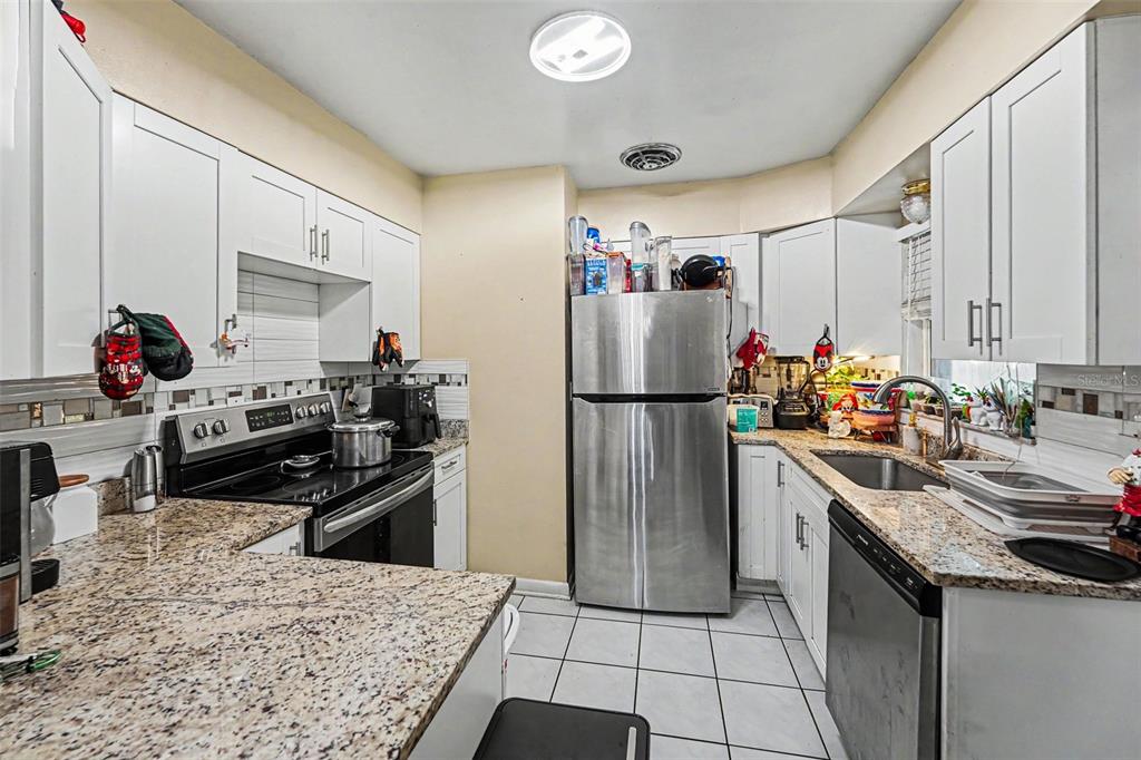 A kitchen features white cabinets, granite countertops, stainless steel appliances, and white tile flooring — 110 N JUPITER AVENUE, CLEARWATER, FL