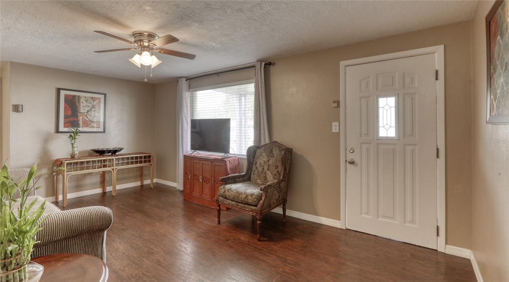 A living room features dark wood flooring, a ceiling fan, and a front entry door — 2048 MELODY DRIVE, HOLIDAY, FL