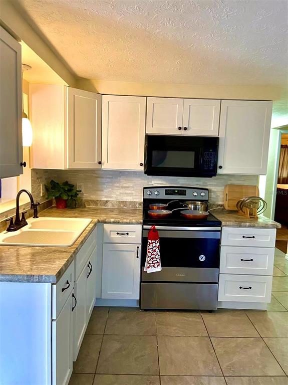 A kitchen features white cabinets, a stainless steel stove, a microwave, and light-colored countertops — 2048 MELODY DRIVE, HOLIDAY, FL