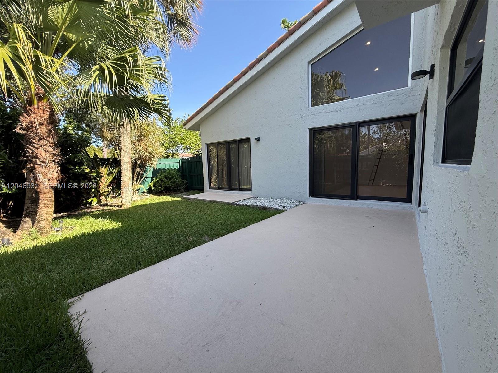 A concrete patio sits outside a white house with large sliding glass doors and windows — 20910 Estada Ln, Boca Raton FL 33433, BOCA RATON, FL