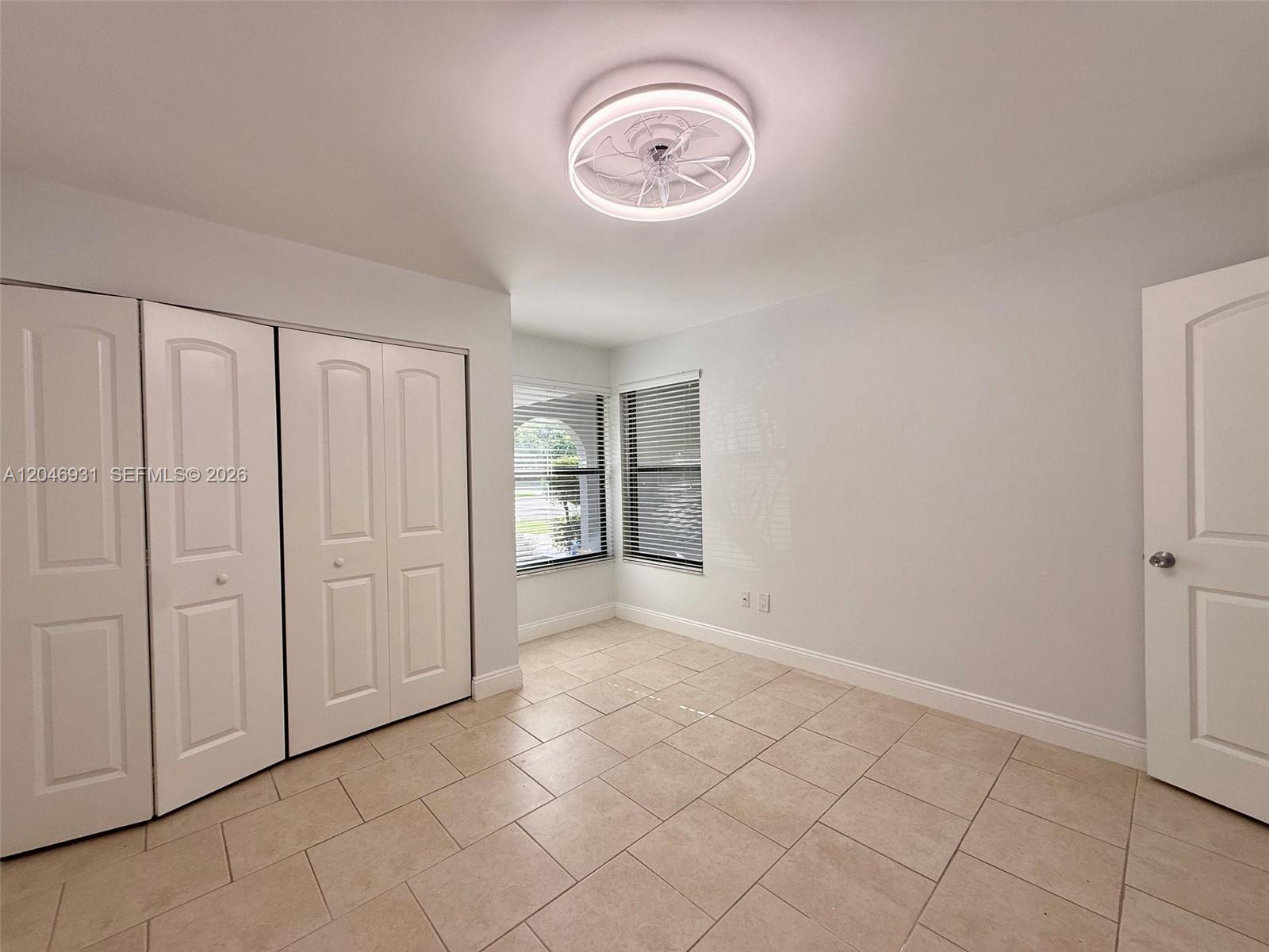 An empty room features white walls, tile flooring, a ceiling fan, and white closet doors — 20910 Estada Ln, Boca Raton FL 33433, BOCA RATON, FL