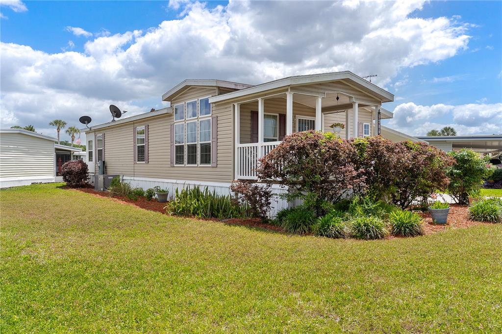 A tan manufactured home with a screened front porch sits on a grassy lot — 2417 VINDALE ROAD, TAVARES, FL