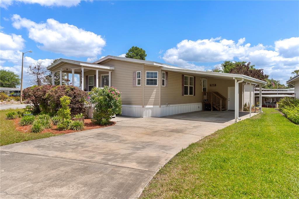 A tan mobile home features a concrete driveway, a carport, and a front porch — 2417 VINDALE ROAD, TAVARES, FL