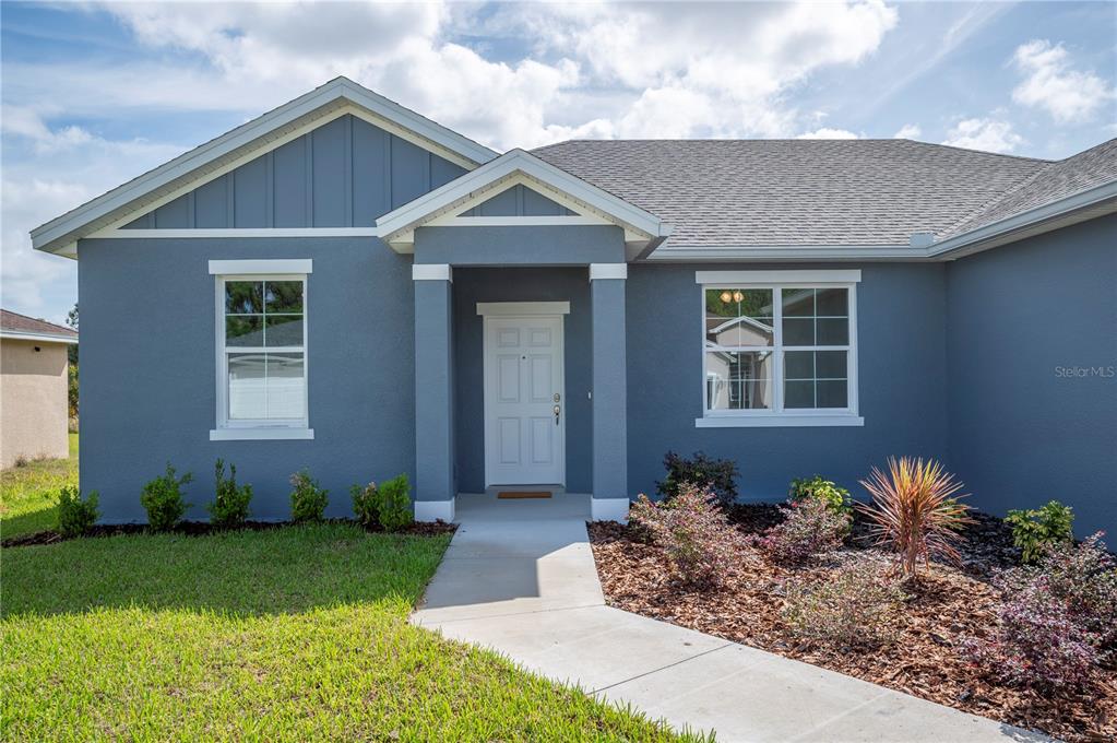 A blue single-story house features a white front door, a concrete walkway, and landscaping — 4550 FAIRWAY OAKS DRIVE, MULBERRY, FL