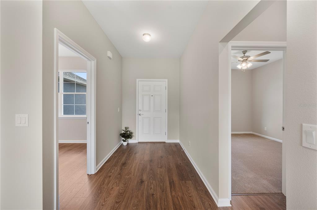 A hallway with wood-look flooring leads to a front door between two open rooms — 4550 FAIRWAY OAKS DRIVE, MULBERRY, FL