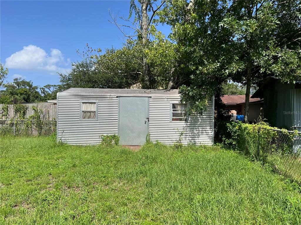 A detached metal storage shed sits in a grassy backyard under a large tree — 5145 SAGINAW AVENUE, JACKSONVILLE, FL