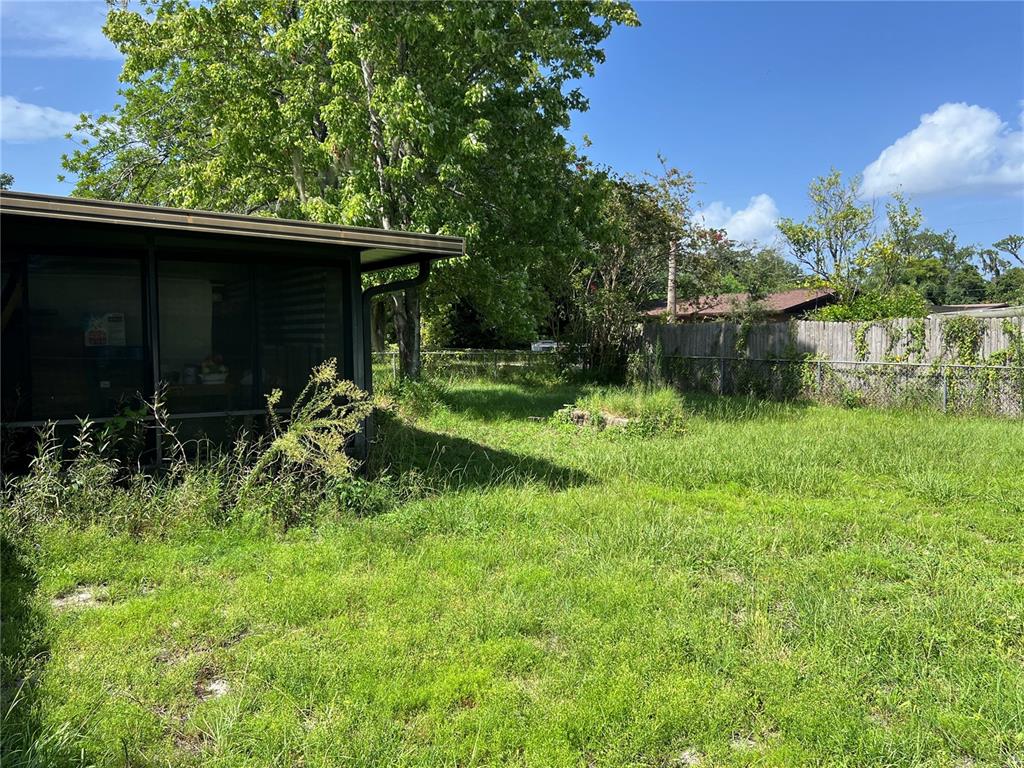 A view of a grassy backyard with a screened-in porch and a wooden fence — 5145 SAGINAW AVENUE, JACKSONVILLE, FL