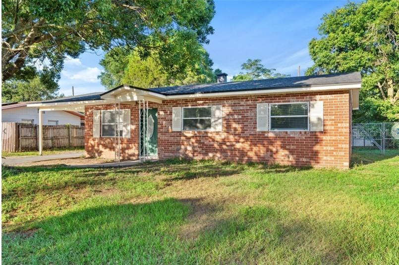 A single-story brick house with a front porch and a carport under a blue sky — 3544 COLLEEN DRIVE, LAKELAND, FL
