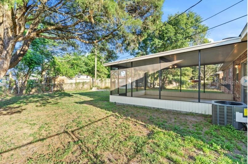 A backyard features a large screened-in porch, a brick exterior wall, and a central air unit — 3544 COLLEEN DRIVE, LAKELAND, FL