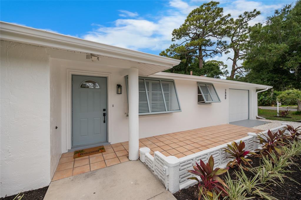 A white house exterior features a light blue front door, tiled porch, and louvered shutters — 2480 MANASOTA BEACH ROAD, ENGLEWOOD, FL