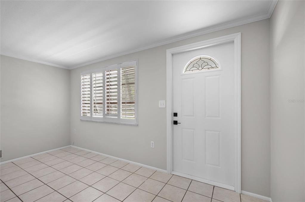 A room with light gray walls, white tile flooring, a window with shutters, and a door — 2480 MANASOTA BEACH ROAD, ENGLEWOOD, FL