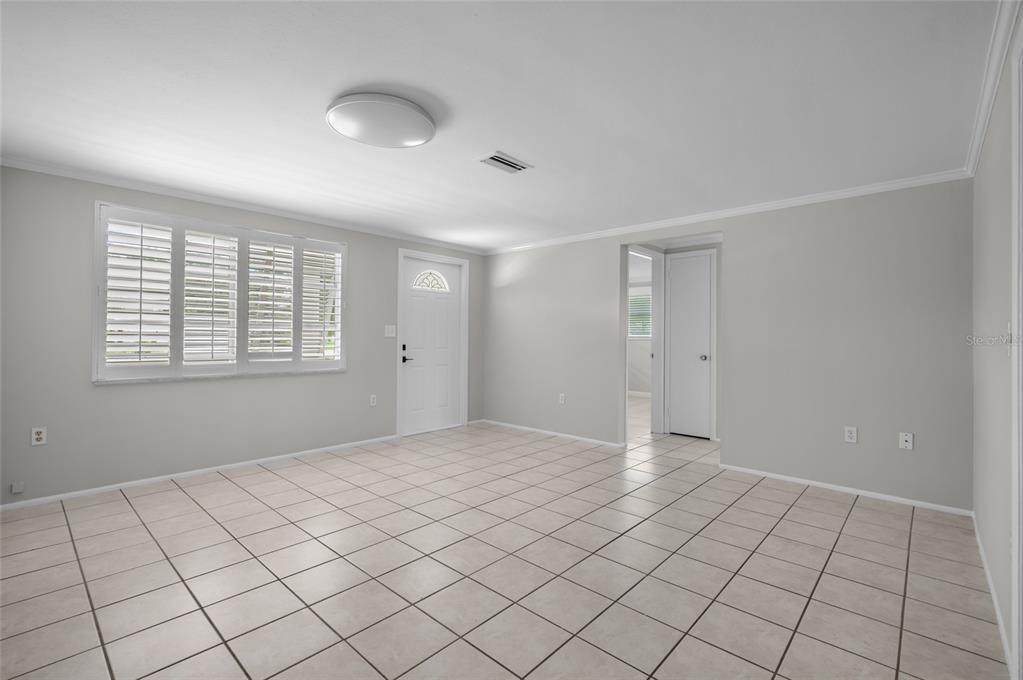 A bright, empty room with light gray walls, white tile flooring, and plantation shutters — 2480 MANASOTA BEACH ROAD, ENGLEWOOD, FL