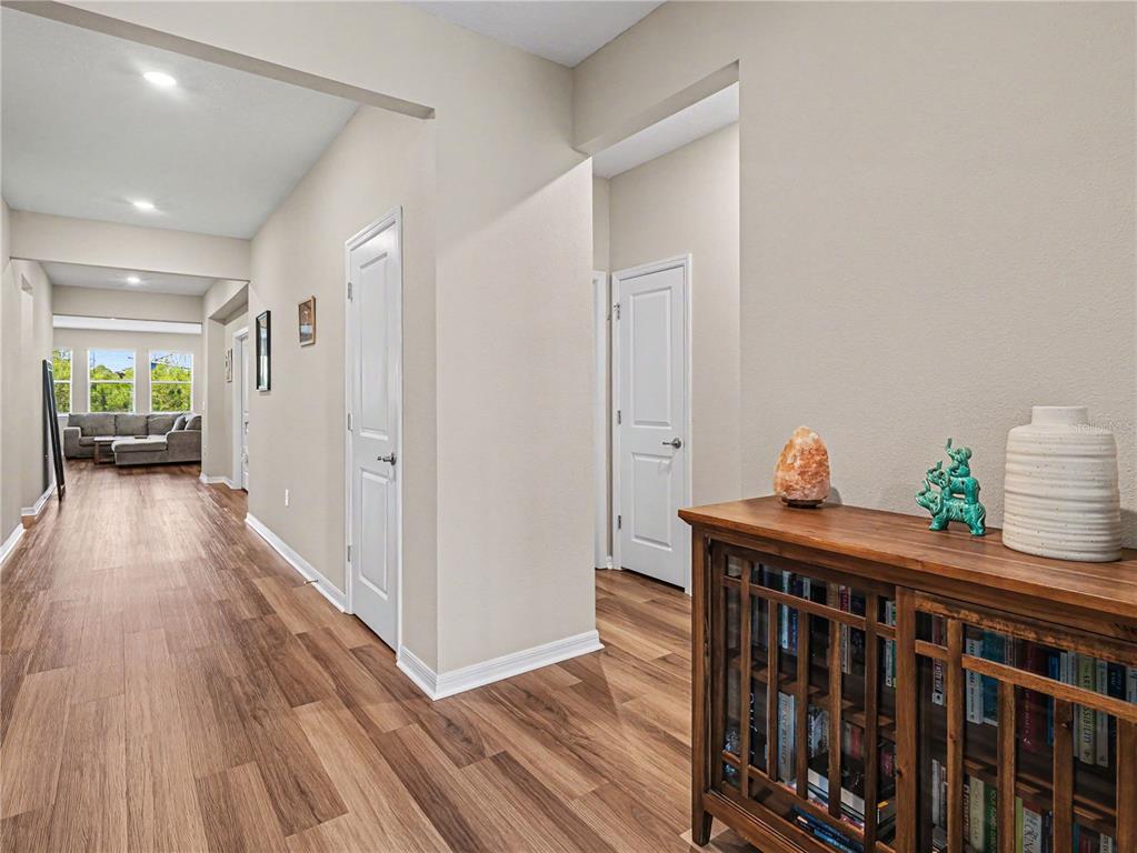 A hallway with wood-look flooring leads to a living area with a gray sectional sofa — 293 DAYLILY BOULEVARD, NOKOMIS, FL