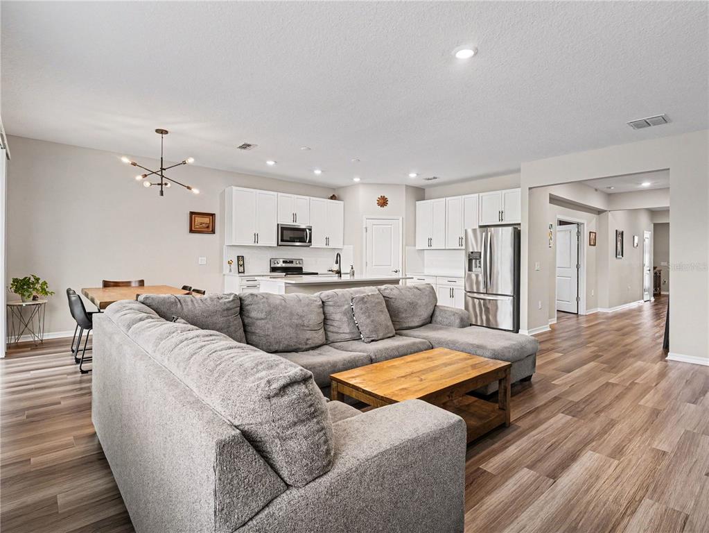 An open-concept living room and kitchen feature gray sectional seating, wood flooring, and white cabinetry — 293 DAYLILY BOULEVARD, NOKOMIS, FL