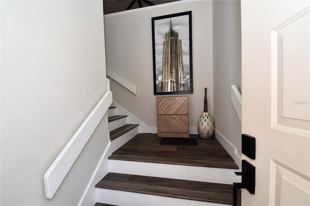 An entryway features dark wood-look stairs, a small wooden cabinet, and a framed skyscraper print — 1631 STARLING DRIVE UNIT 204, SARASOTA, FL