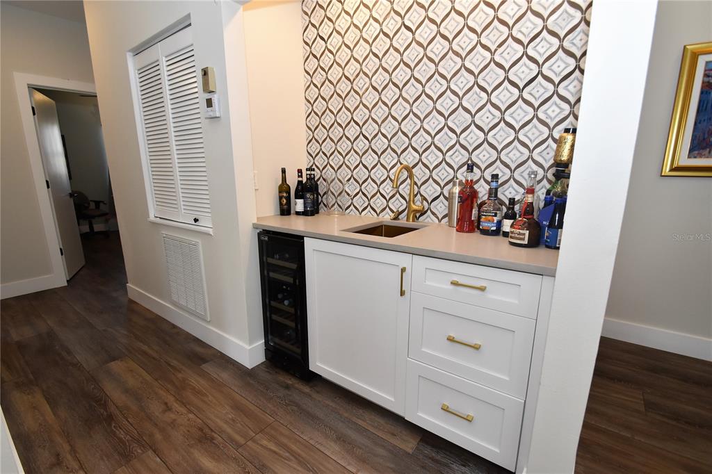 A wet bar features white cabinetry, a wine cooler, a gold faucet, and patterned tile backsplash — 1631 STARLING DRIVE UNIT 204, SARASOTA, FL