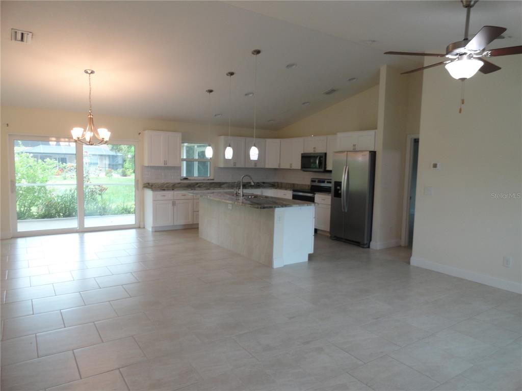 An open-concept kitchen features white cabinets, a granite-topped island, and light tile flooring — 2580 VOGLER LANE, NORTH PORT, FL