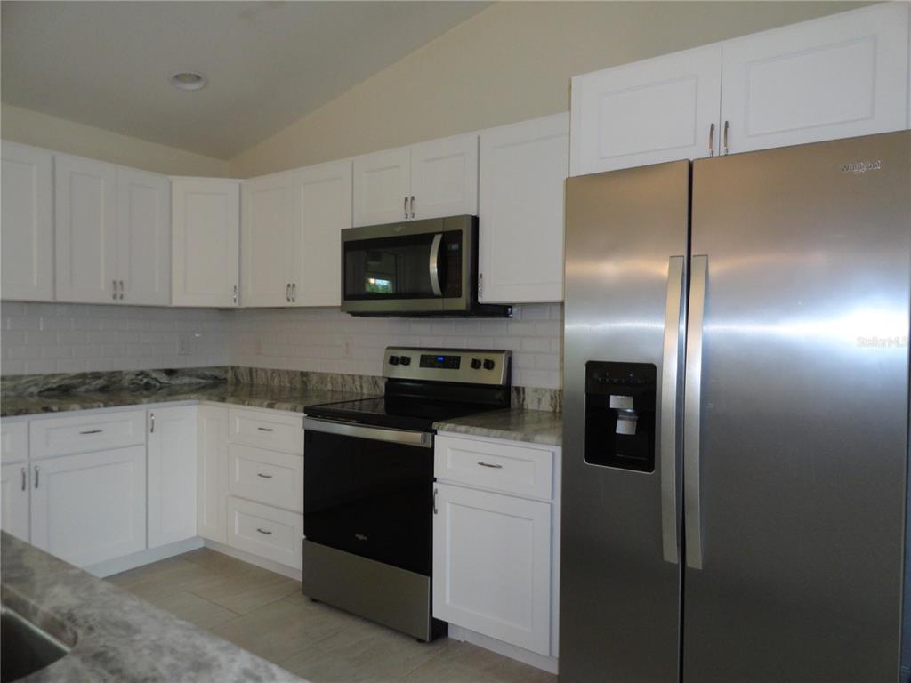 A kitchen features white cabinets, stainless steel appliances, and granite countertops with a tile backsplash — 2580 VOGLER LANE, NORTH PORT, FL