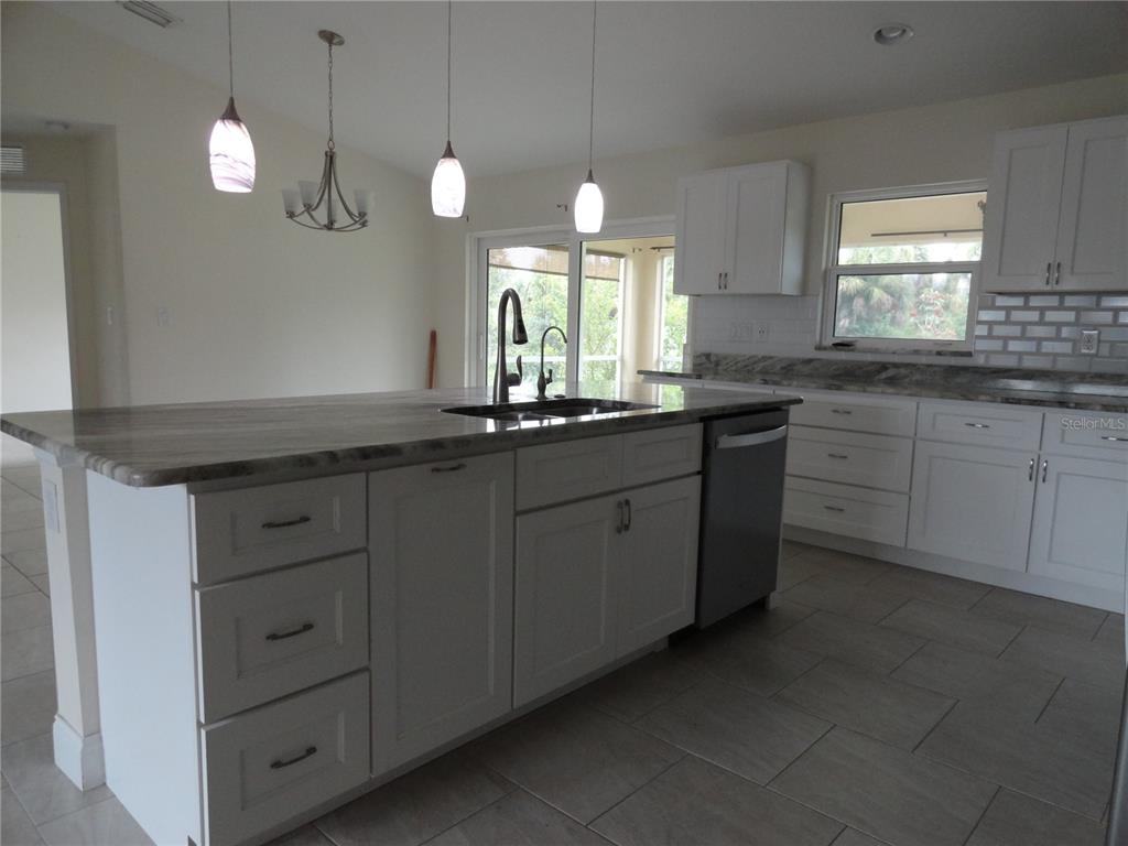 A kitchen features a white island with a sink, stone countertops, and pendant lighting — 2580 VOGLER LANE, NORTH PORT, FL