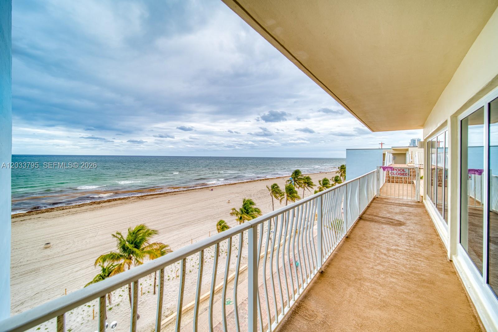 A balcony overlooks a sandy beach and the ocean under a cloudy sky — 300 Oregon St # 507, Hollywood FL 33019, HOLLYWOOD, FL