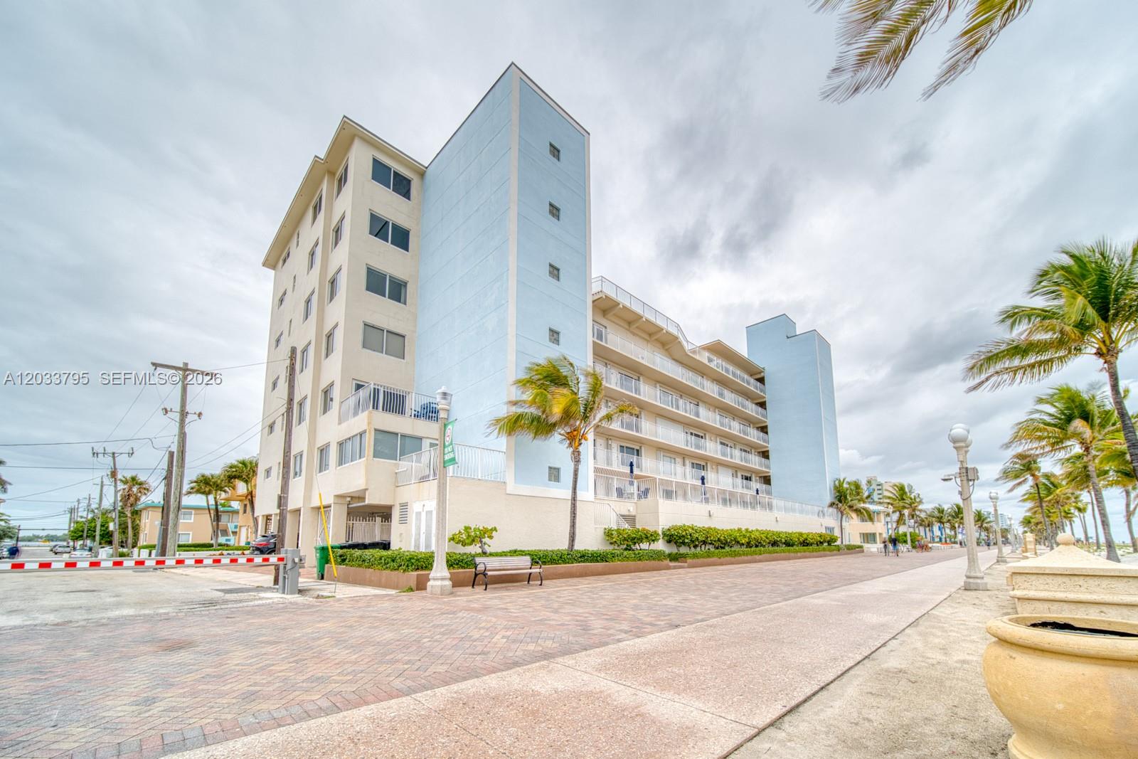 A multi-story light blue and beige apartment building stands next to a paved boardwalk — 300 Oregon St # 507, Hollywood FL 33019, HOLLYWOOD, FL
