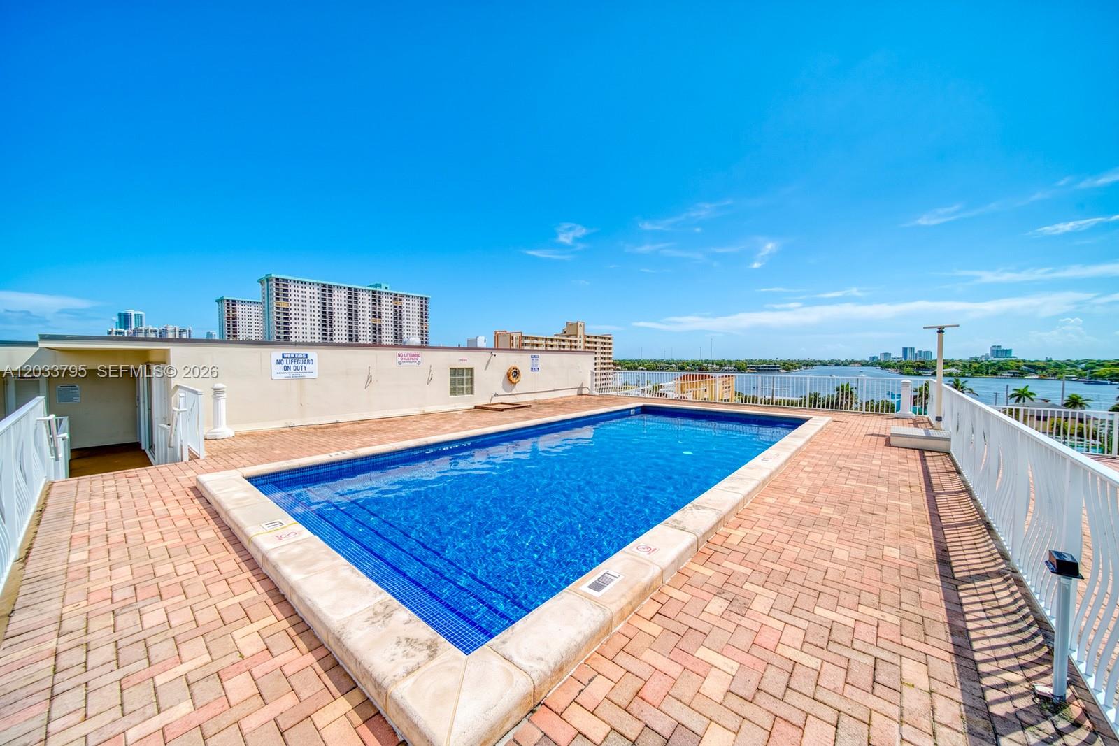 A rectangular rooftop swimming pool is surrounded by a brick patio and white railings — 300 Oregon St # 507, Hollywood FL 33019, HOLLYWOOD, FL