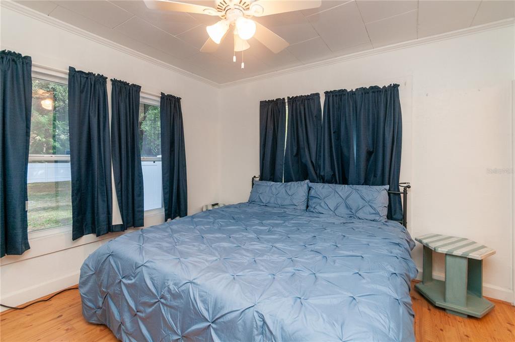 A bedroom features a bed with blue bedding, dark curtains, and a ceiling fan — 1235 BASS BOULEVARD, DUNEDIN, FL