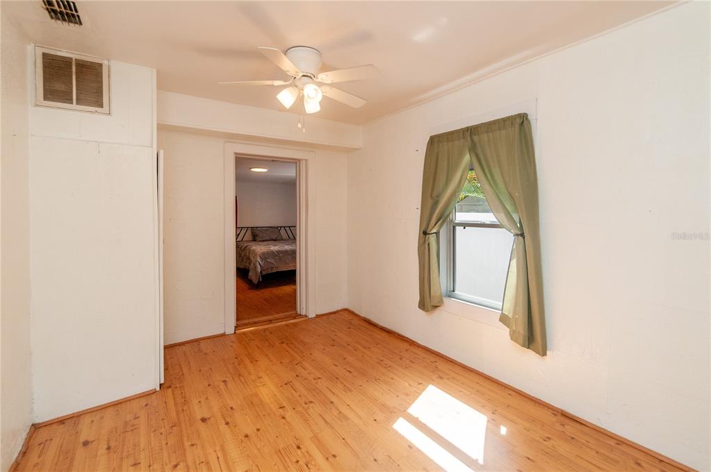 An empty room with hardwood floors, a ceiling fan, and a doorway leading to a bedroom — 1235 BASS BOULEVARD, DUNEDIN, FL