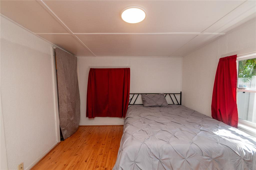 A bedroom features wood flooring, a bed with a grey comforter, and red curtains — 1235 BASS BOULEVARD, DUNEDIN, FL