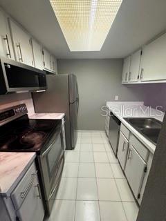 A galley kitchen features white cabinets, stainless steel appliances, and light-colored tile flooring — 1871 PINE CONE CIRCLE UNIT 1, CLEARWATER, FL