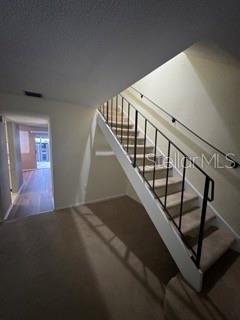An interior view shows a carpeted room with a staircase featuring a black metal railing — 1871 PINE CONE CIRCLE UNIT 1, CLEARWATER, FL