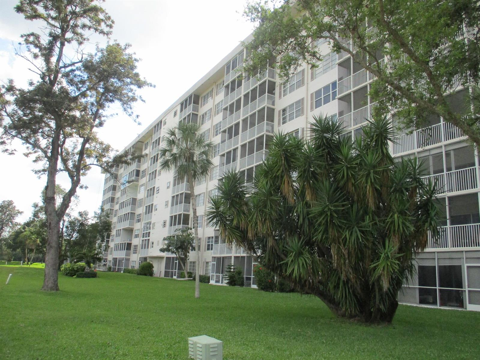 A multi-story apartment building with screened balconies sits on a grassy lawn with trees — 3300 N Palm Aire Drive # 306, Pompano Beach FL 33069, POMPANO BEACH, FL