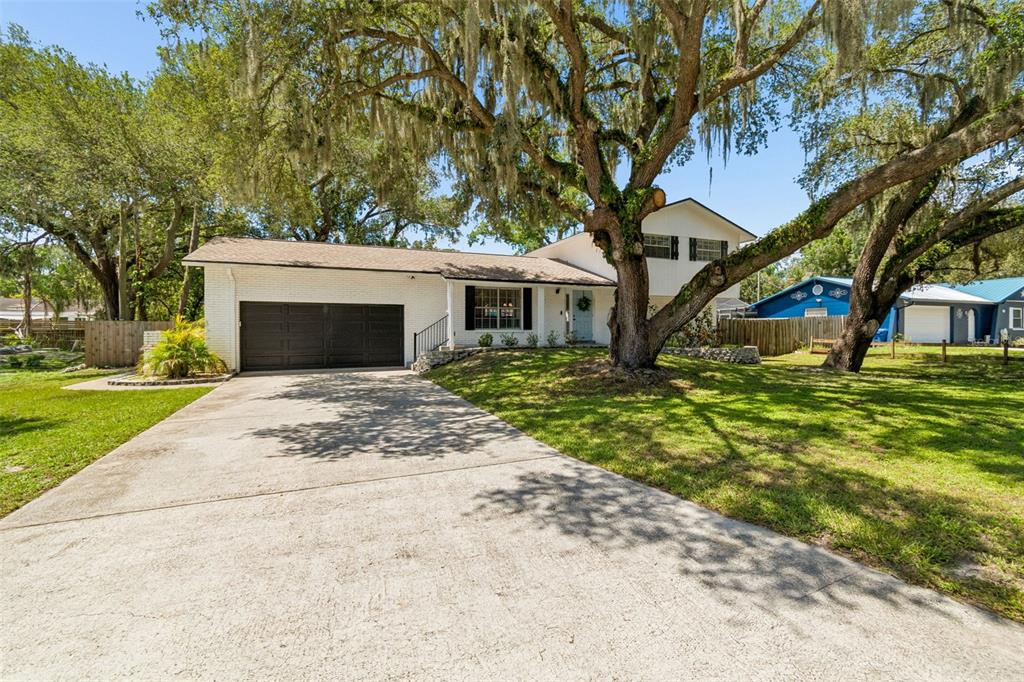 A white brick house with a dark garage door sits behind a large oak tree — 114 WINDY CIRCLE, BRANDON, FL