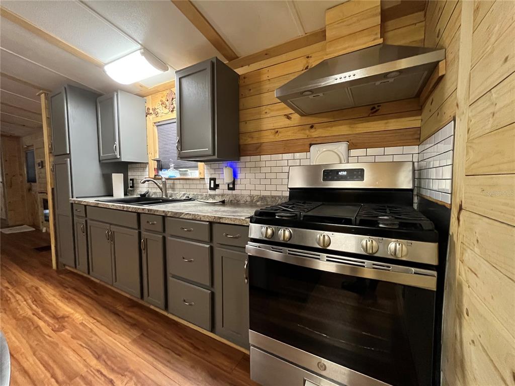 A kitchen features gray cabinets, a stainless steel gas range, and wood-paneled walls — 124 W PARKER AVENUE, BUSHNELL, FL