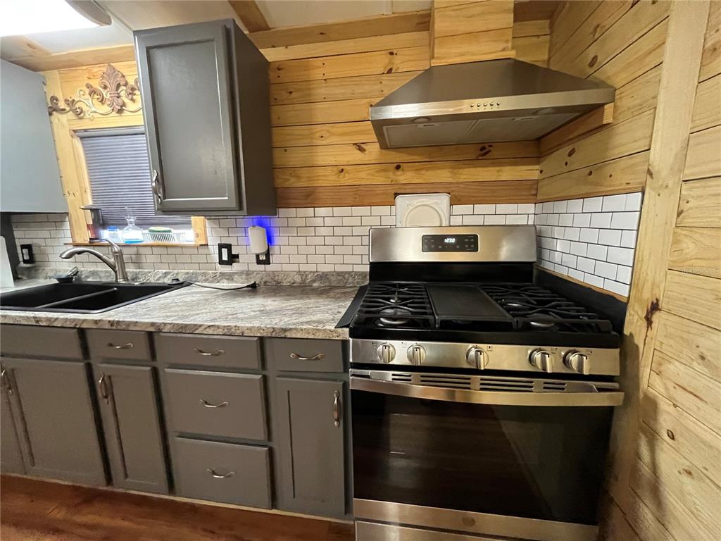 A kitchen features gray cabinets, a stainless steel gas range, and wood-paneled walls — 124 W PARKER AVENUE, BUSHNELL, FL